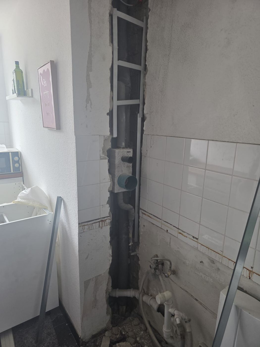 Aufgestemmter Installationsschacht mit offenen Leitungen neben der Küchenspüle nach einem Wasserschaden